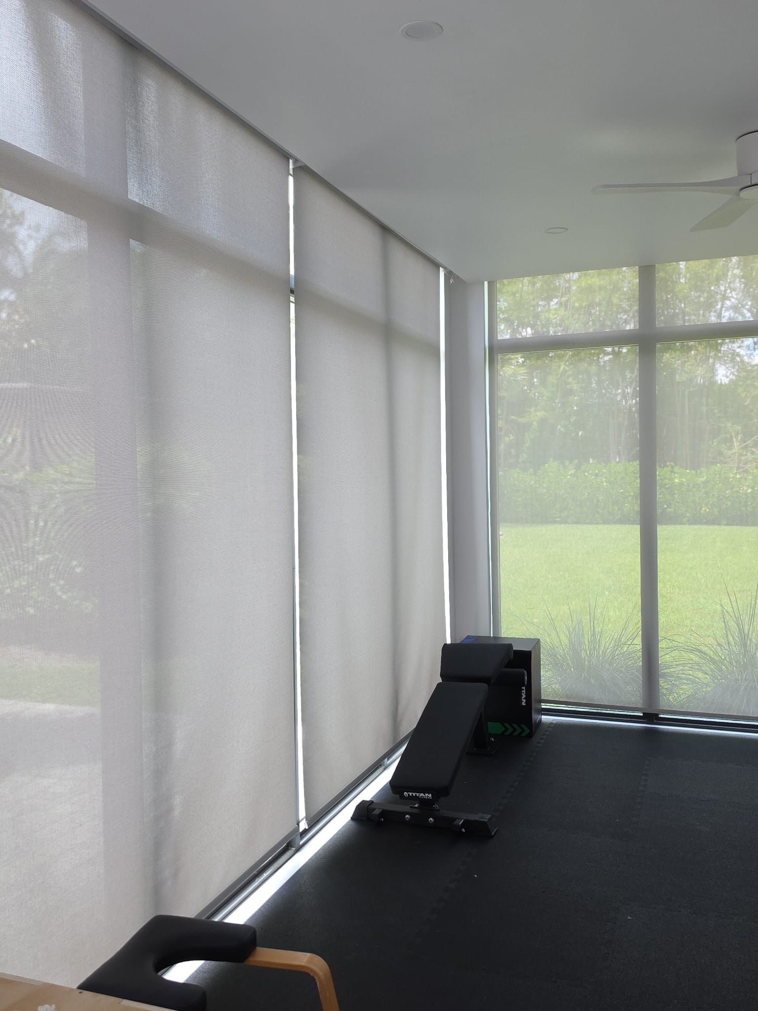Floor-to-ceiling roller shades in a home gym with screened windows