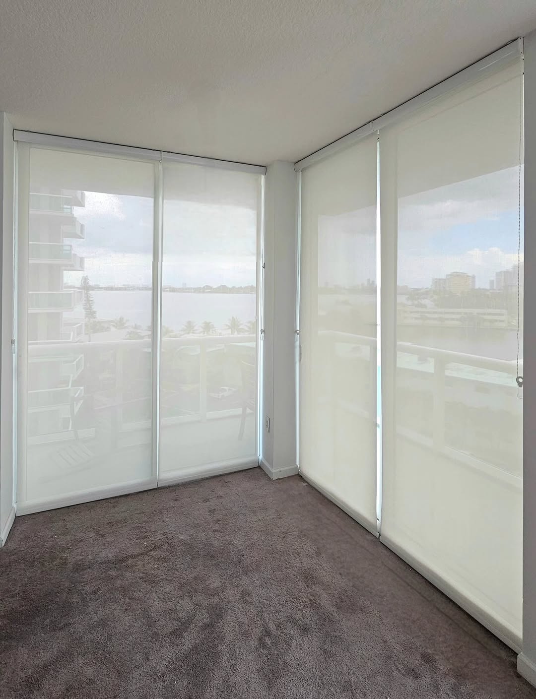 White roller shades on a corner window wall overlooking water