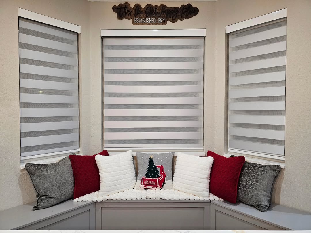 Three grey zebra blinds over a bay window seat